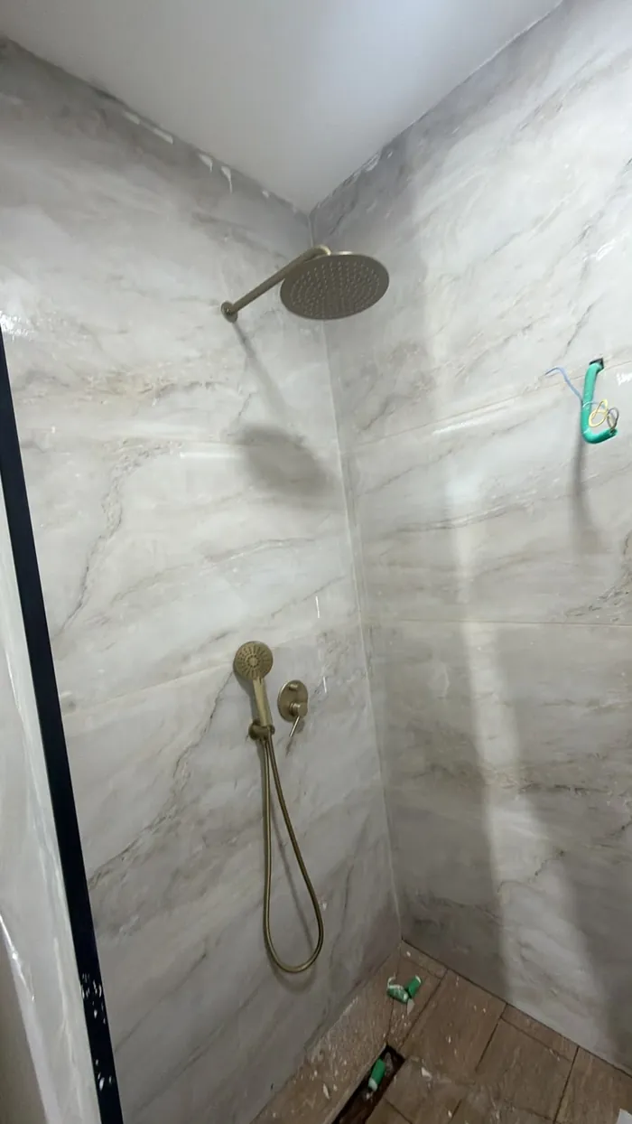 מקלחון מוגמר בחיפוי טקסטורת אבן בגוון בז' וגוף מקלחת גשם.
