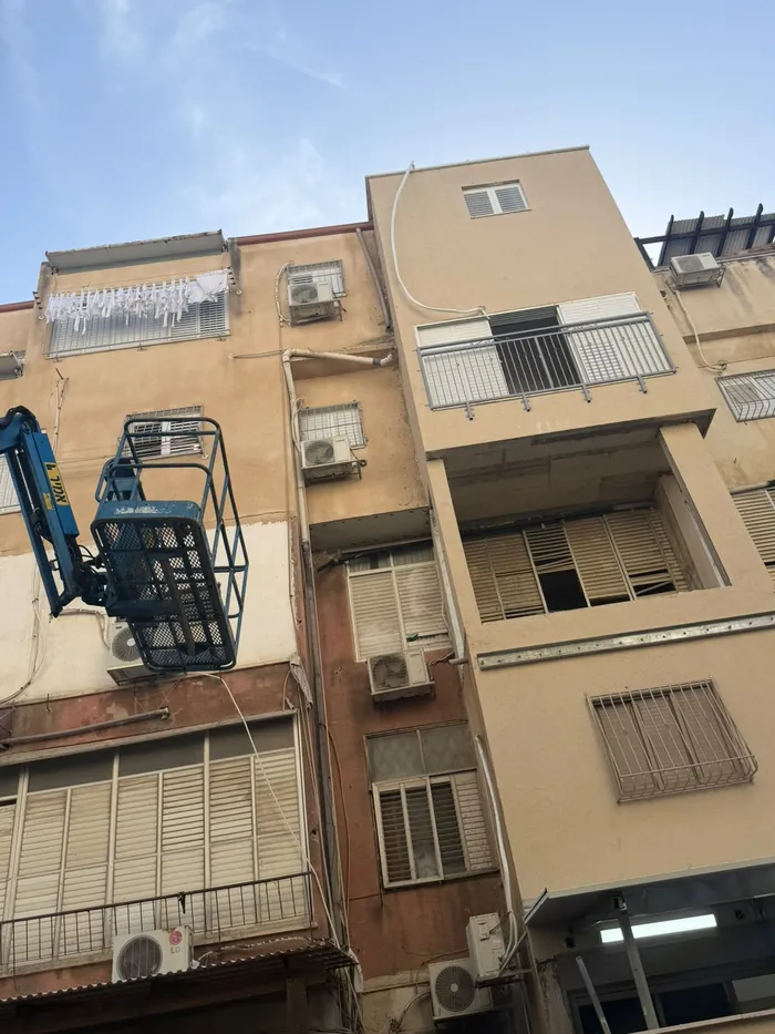 עבודות בחזית בניין מגורים עם סולם ופיגום ברחוב.