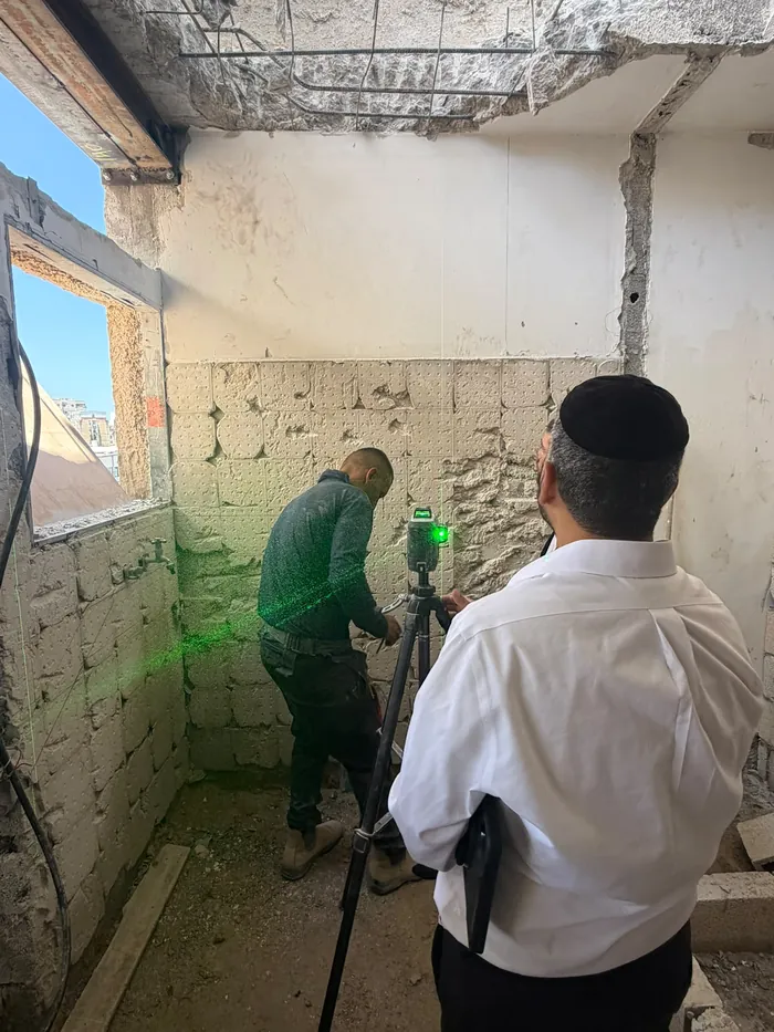 עובד מסיר טיח פגום מקיר ומטפל ברטיבות לפני צבע.